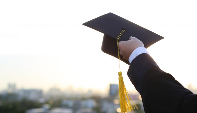 A picture of a man holding a graduation hat - stock photo GettyImages-1271093884