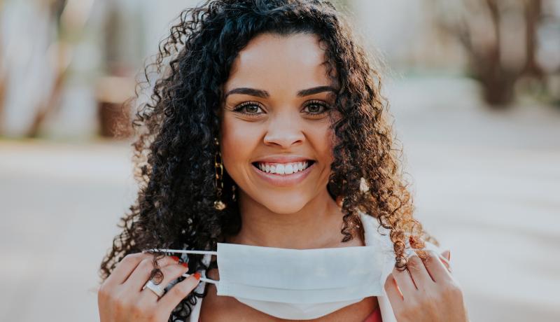 Woman removing face protection mask and smiling - stock photo GettyImages-1267548377