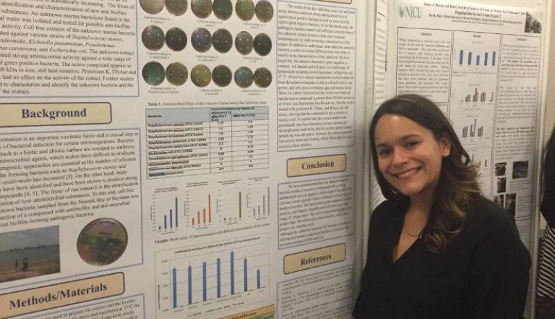 NJCU senior Jenique Klinkerth with a large poster detailing her biology research on the antibacterial properties of marine bacteria