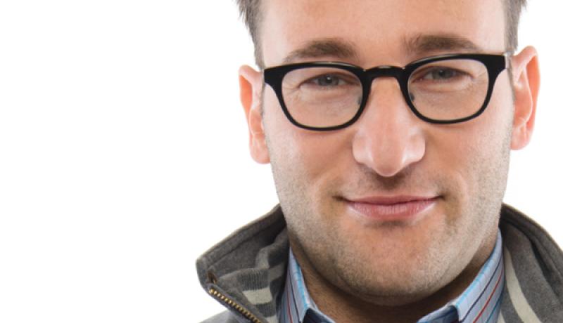 portrait of a young Caucasian male with black-framed glasses dressed in a gray jacket with a blue-collared shirt showing 