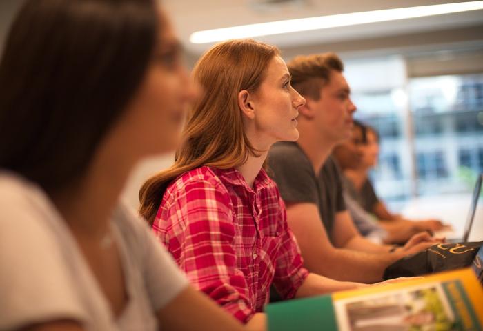 Five students sitting in a row at a table in a classroom