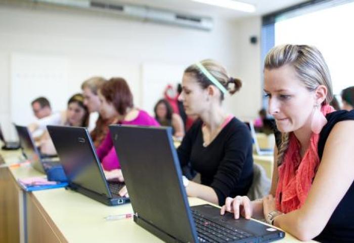 Room full of students sitting at rows of long desks on laptop computers.