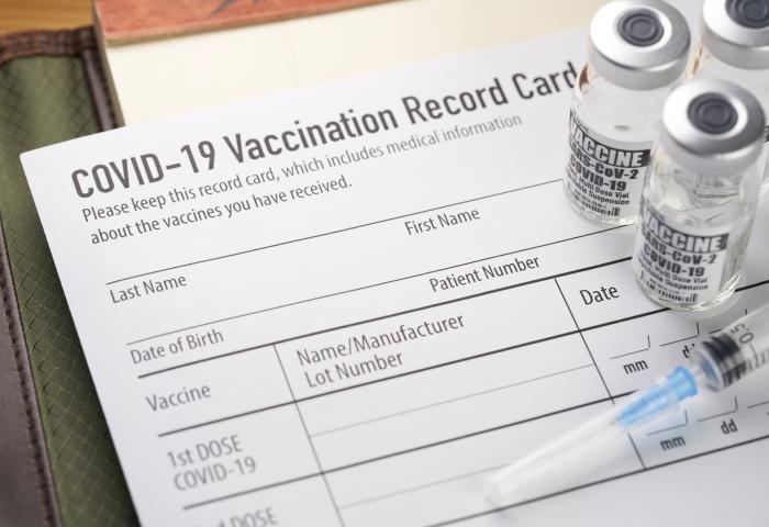 Covid-19 vaccination record card with vials and syringe. - stock photo GettyImages-1289454645