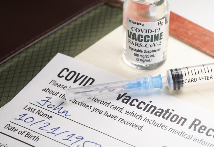 Covid-19 vaccination record card with syringe and vial - stock photo GettyImages-1298051782