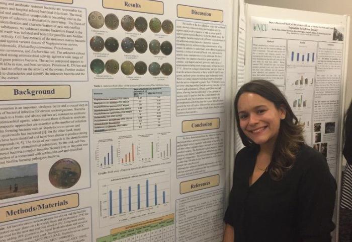 NJCU senior Jenique Klinkerth with a large poster detailing her biology research on the antibacterial properties of marine bacteria