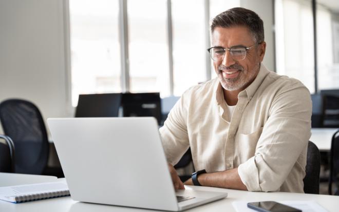 older man uses laptop smiling