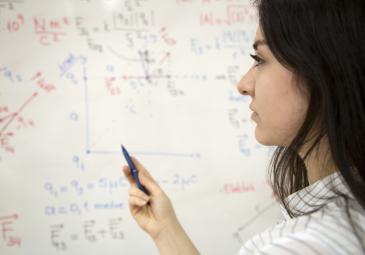 female math student working out equations on whiteboard
