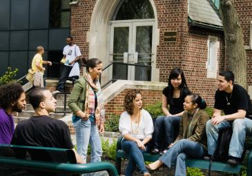 Group of students sitting on benches outside building 