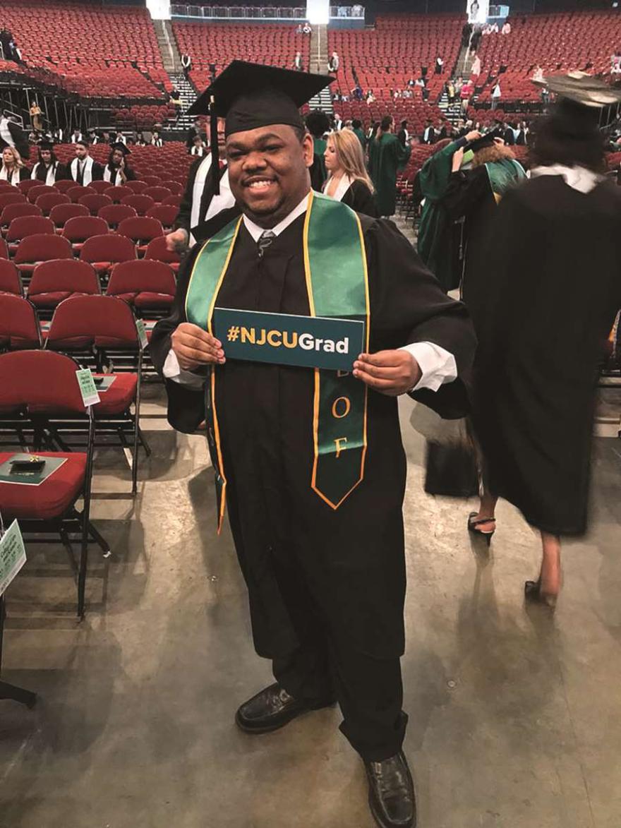 Graduate holding up #NJCUGrad sign.