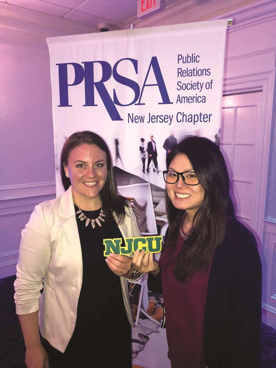 Nicole and Thi hold NJCU in front of PRSA New Jersey Chapter banner.