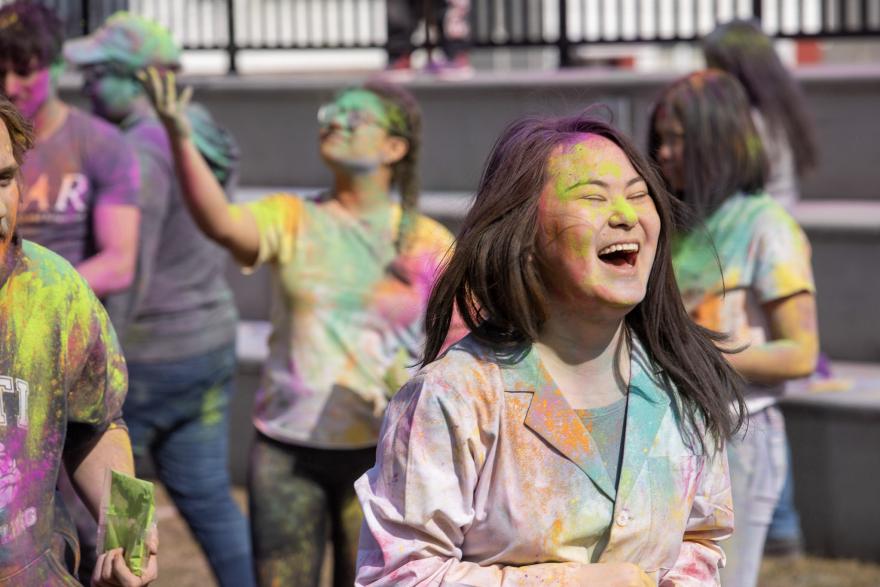 Girl in crowd covered in paint laughing at Holi event