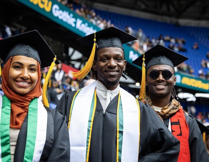 graduates at commencement 2 men, 1 woman of color
