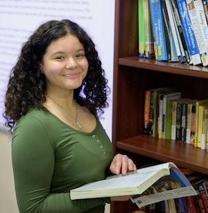 girl stands art bookshelf with book in hand