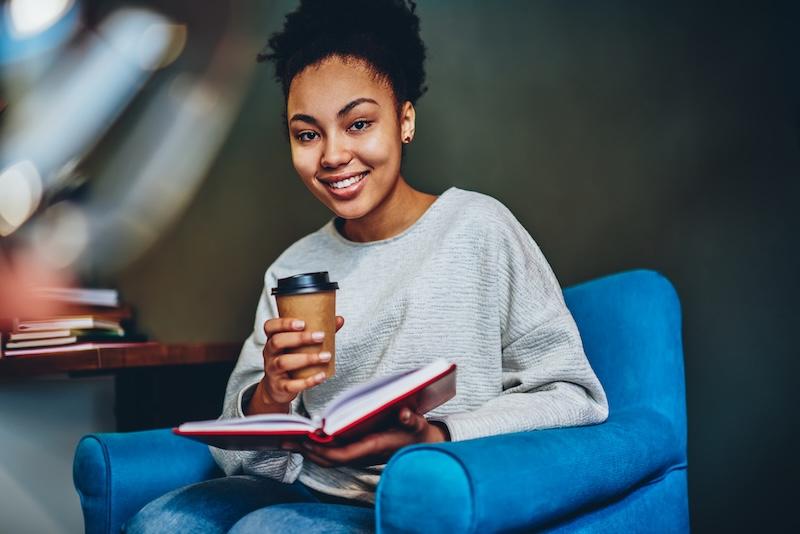 woman smiling seated holding coffee cup and book