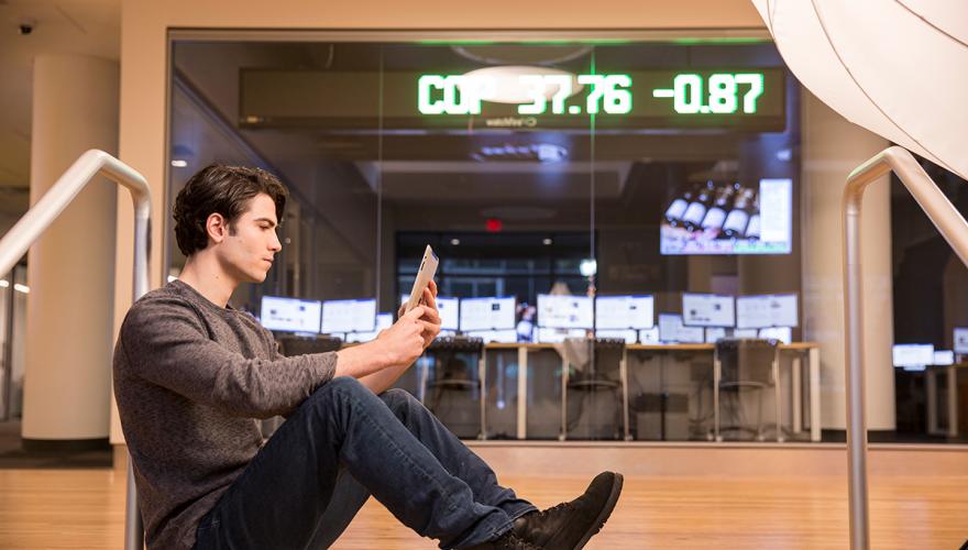 male student sitting in front of bloomberg terminal in the school of business