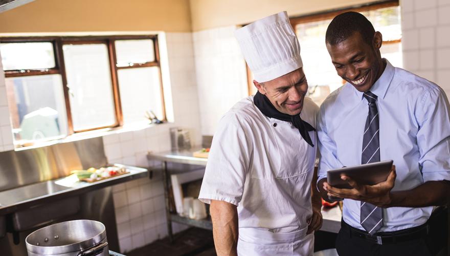 Two men discussing business in kitchen of restaurant.