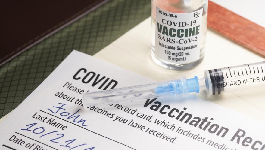 Covid-19 vaccination record card with syringe and vial - stock photo GettyImages-1298051782