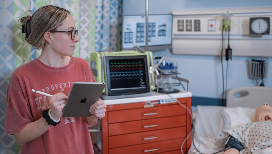 Nursing student with iPad and defibrillator in lab