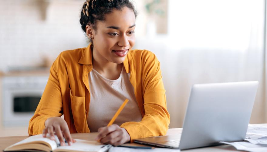 Woman looking at laptop and writing something down