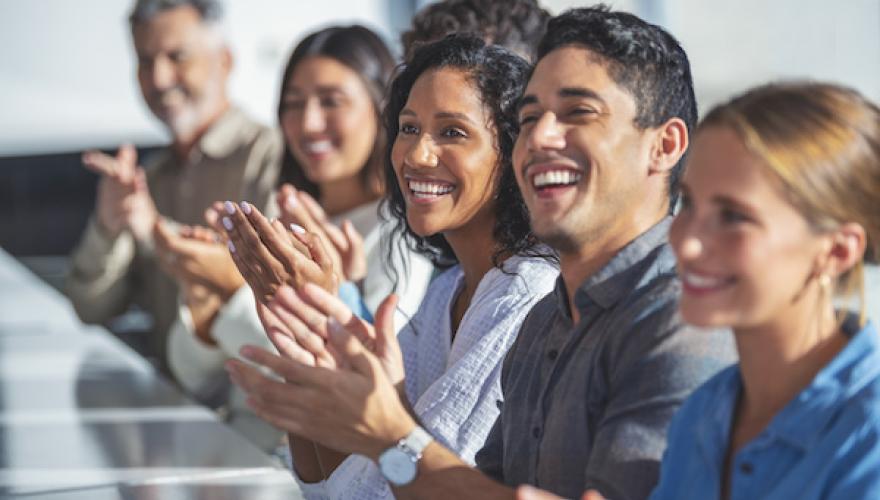 SMILING CLAPPING PEOPLE AT CONFERENCE TABLE