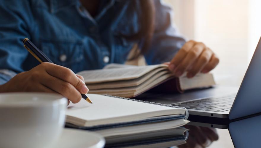 WOMAN WRITING ON NOTEBOOK WITH LAPTOP