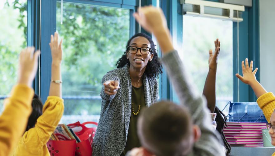 FEMALE TEACHER POINTS TO YOUNG STUDENTS
