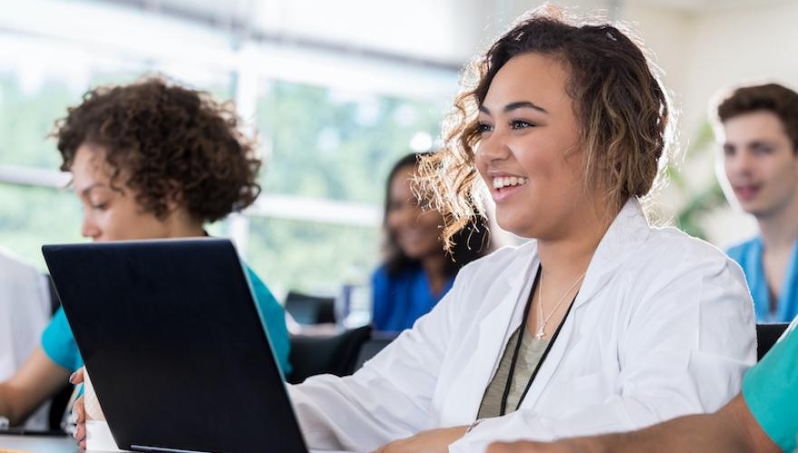 WOMAN AT CLASSROOM DESK WITH LAPTOP