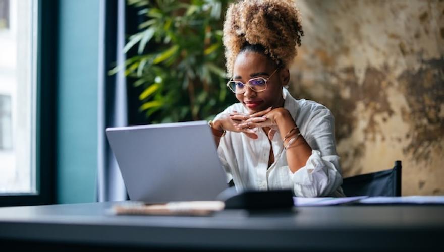 woman at desk looks at laptop