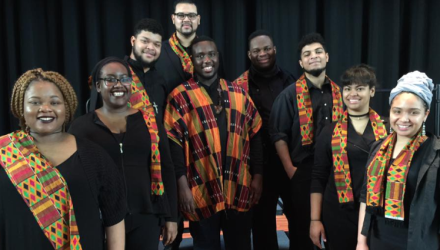 9 ensemble members standing in a v formation with a drum in the middle
