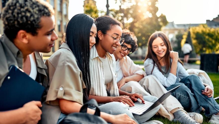 students seated on grass with laptop
