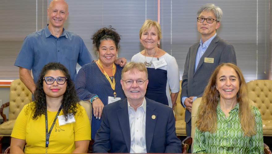 Seven people, three sitting in front, four standing in back