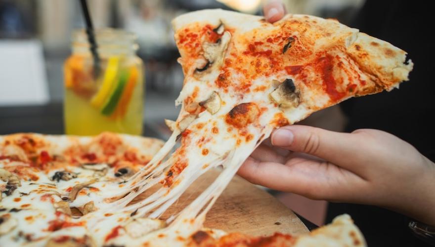 hands taking a slice of pizza