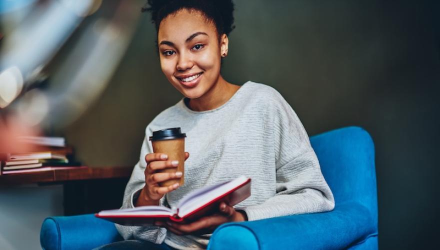 woman smiling seated holding coffee cup and book