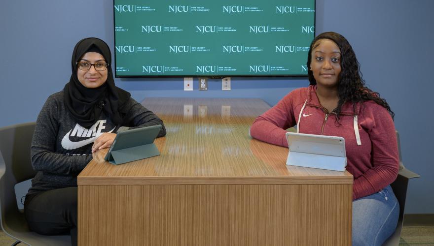 Sonyia Yar and Jenny Joachim ABSN Students with iPads at table with NJCU screen behind them