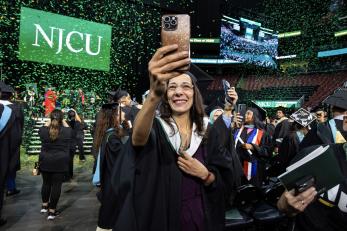 A graduate take a selfie with green and gold confetti falling in the background